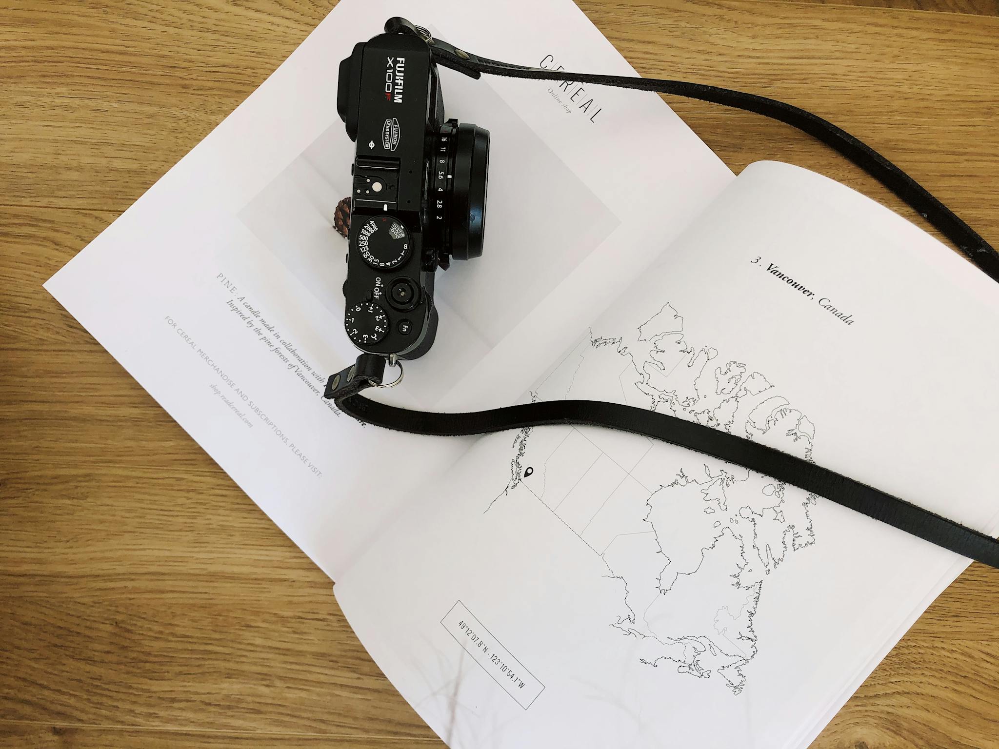 Overhead shot of a classic camera placed on an open book with a world map, on a wooden table.